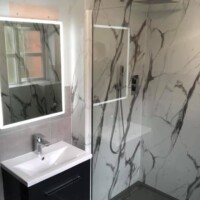 Marble effect wall panelling with slate grey shower tray, wall-hung basin unit, concealed shower and LED mirror