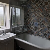 Traditional free-standing bath with traditional shower valve, patterned wall tiling and traditional furniture