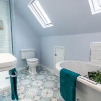 Vaulted ceiling ensuite featuring free-standing bath, traditional toilet, basin and pedestal and frameless shower with patterned floor