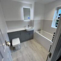 Modern fitted furniture run with recessed bathtub, half-height tiling, click lock flooring and LED mirror