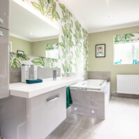 Disabled wet room featuring tiled in bath with decorative LED lighting, wall-hung basin unit with bespoke basin and leaf print wallpaper
