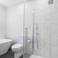 Frameless shower enclosure with close coupled toilet and back-to-wall freestanding stone bath with marble effect tile