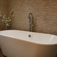 Free-standing bathtub with freestanding brushed stainless steel bath filler and decorative tiles