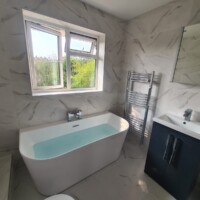 Back-to-wall freestanding bath with a floor-standing basin unit, chrome ladder rail and marble effect tiles