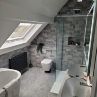 Bathroom with vaulted ceiling including a wall-hung toilet, walk-in shower, free-standing countertop bowls, and recessed alcove